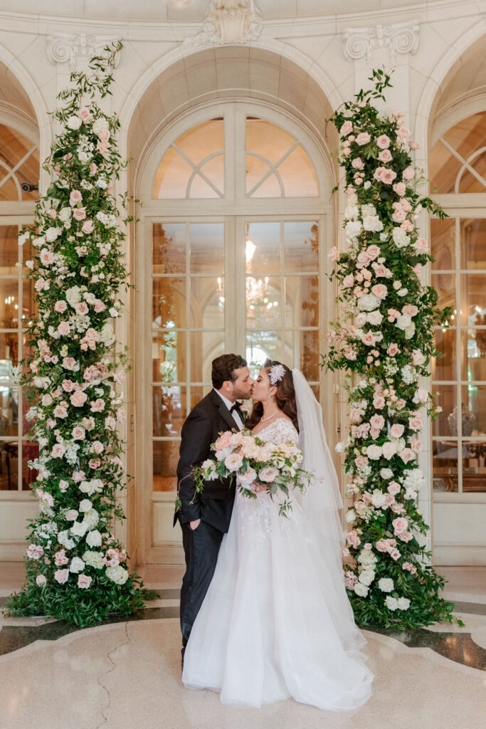 Bride and groom kissing with blush and ivory floral arch in background