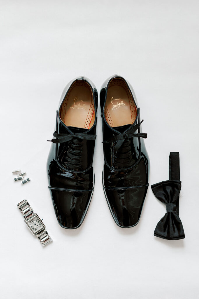 Flat lay of groom's dress shoes, bowtie, watch, and cuff links