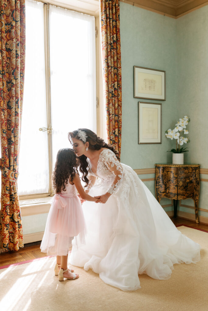 Bride holding hands with flower girl and kissing her on the forehead