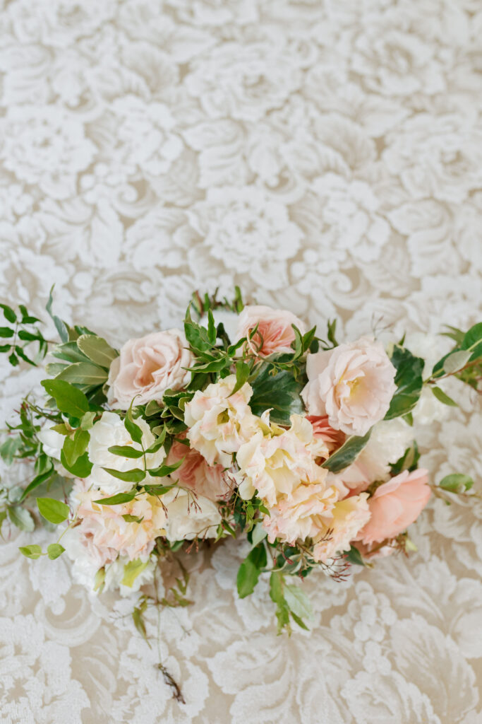 Blush and ivory bridal bouquet with greenery on a lace backdrop